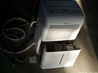 Front view of the Classic dehumidifier showing the removable water collection tank pulled out, the drain hose coiled beside it, and the overall unit in good physical condition.