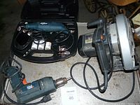Photo showing Black and Decker electric drill, 7¼ inch Skill Saw, and rotary tool with case and accessories on a surface.