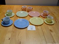 Overview photo showing entire 14-piece pastel milk glass children's tea set including cups, saucers, luncheon plates, creamer, and sugar bowl arranged on wood table.