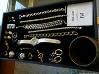 Top view of jewelry items on black felt including bracelets, earrings, rings, pins, money clip, watch with white strap