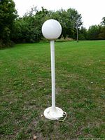 Full view of mid-century modern style white plastic pole lamp with round globe shade and circular base on grass outdoors.