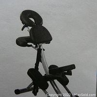 Foldable massage chair fully assembled with padded black cushions for headrest, chest, armrests, and knees supporting user's seated position for massage.