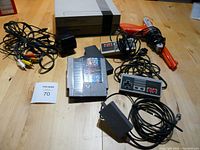 Original Nintendo Entertainment System console with controllers, NES Zapper gun, power adapter, AV cables, and game cartridge arranged on a wooden surface.