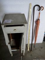Small homemade wooden cabinet shown from the front and side angles, with visible drawer and door, showing signs of wear and some structural aging.