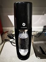Black SodaStream machine with a bottle attached showing water with carbonation bubbles inside.