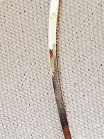 Close-up photo showing the flat, smooth herringbone pattern of the sterling silver chain on a grey textured fabric background.