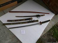 Overview of two decorative swords with black and gold dragon pattern sheaths and wooden sheath on white surface.