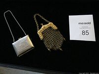Two vintage metal coin purses placed on a black surface with a MaxSold lot number card.