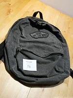 Full view of the black Vans canvas backpack showing its overall shape and front zip pocket.