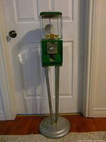 Full view of the green Gabrielle gumball machine on metal stand against a door.