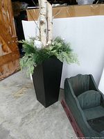 Photo showing large black planter with greenery, birch branches, and lights, next to wooden sleigh on floor.
