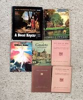 Seven art books laid out on carpet: A Bécsi Képtár II, George Inness, William Blake, Canaletto and His Pictures, Guy Pene Du Bois, Charles Demuth, and one additional book with brown cover.