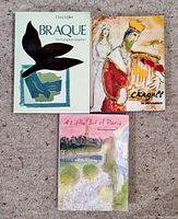 Three art books displayed flat on a carpet: Braque by Dora Vallier, Chagall in Jerusalem, and A Little Bit of Paris by Jean-Jacques Sempé.