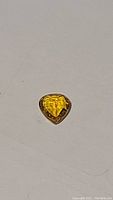 Photo showing heart-shaped golden orange sapphire gemstone reflecting light and showing facets clearly.