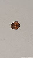 Heart-shaped deep orange spessartite garnet gemstone on a plain light background, showing surface facets and color.