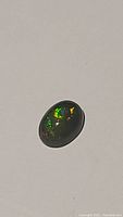 Oval natural black Ethiopian opal with vibrant green, yellow, and red flashes on white background.