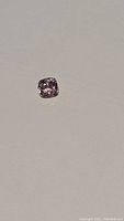 Close-up of a small, square-ish cushion cut pink spinel gemstone against a plain background, showing color and cut details.