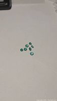 Seven natural emerald gemstones in varying sizes laid out on white background for size reference.