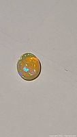 Oval cabochon cut Ethiopian opal on a flat surface showing play of colors.