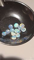 Multiple loose round calibrated Ethiopian opal stones in a black container showing their base white opalescence and flashes of color.
