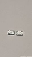 Two rectangular emerald cut aquamarine stones side by side on a light background.