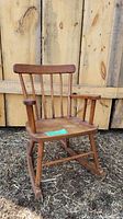 Front view of antique toddler wooden rocking chair showing vertical spindle backrest, armrests, and rockers.