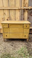 Front view of an antique wooden dresser with yellow paint, showing wear and multiple drawers with round knobs.