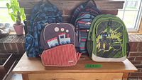 Photo showing all four backpacks arranged on table in front of a window, displaying designs and sizes.