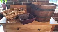 Full view of wooden barrel planter and two wicker baskets on wooden dresser against brick background.
