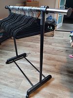 Metal clothes rack with black velvet hangers on wooden floor, showing side view with rack partially extended and hangers aligned