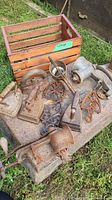 Crate and hand tools including sad irons, meat grinders, trivets, and hand press, showing weathered and rusty surfaces.