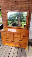 Wood dresser and matching framed mirror placed on a wooden deck against a brick wall.