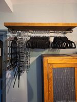 Wide view of various types of hangers hanging on a wooden rod including black velvet and silver hangers.