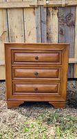 Front view of wooden end table with 3 drawers showing drawer fronts and metal knob handles.