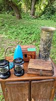 Display of all lot items on wooden surface outdoors showing different decor pieces including lanterns, chest, umbrella holder, wicker box and lamp