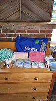 Photo showing array of Norwex products including the blue reusable bag, various cloths, scrub mitt, small bottles and packets arranged on a wooden surface.