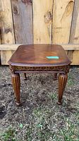 Full view of rectangular wooden side table with ornate carved details and four legs on ground