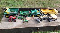 Full view of the sandbox toy vehicles showing John Deere and Tonka metal models including dump trucks, tractors, and loaders placed on outdoor wooden surface.