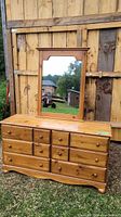Full view of dresser with mirror attached in front of wooden fence