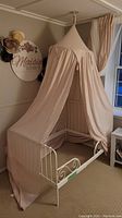 Full view of light pink fabric canopy draping over a child's bed frame in a room, canopy forms a pointed top hanging from the ceiling.