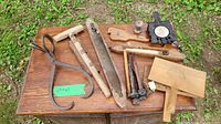 Overview of all tools on wooden table—large ice tongs, wooden mallets, wool carder, and other miscellaneous wooden and metal primitive tools.