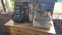 Four bags on wooden dresser beside a window: camouflage bag, brown vegan leather backpack, beige geometric tote, and grey tote bag