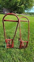 Both red metal saddle racks standing upright on grass showing front and side views