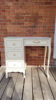 Front view of small off white painted desk with three drawers on the left and one drawer on the right, showing curved legs and decorative drawer fronts.