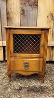 Front view of small vintage wooden side table showing wire mesh door and drawer with decorative metal hardware