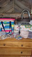 Photo showing the full lot of colorful insulated picnic bag, woven purse, wine gift bag, pouches, lunch bag, and luggage tags on wooden surface.