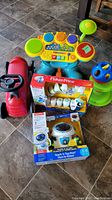 Photo showing the full lot of toddler learning toys including Radio Flyer ride-on, Fisher Price drum kit with stool, shape sorter, and two unopened Fisher Price robot toys in boxes.