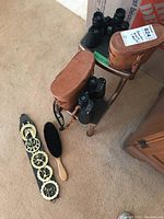 Overview of binoculars, horse brasses, clothing brush, and step stool on carpeted floor.