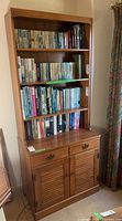 Full front view of wooden bookcase cabinet filled with books on shelves, showing overall size and shape.