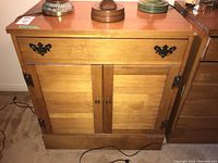 Front view of vintage wooden cabinet showing drawer with black metal handles and two slatted wood doors with brass knobs.